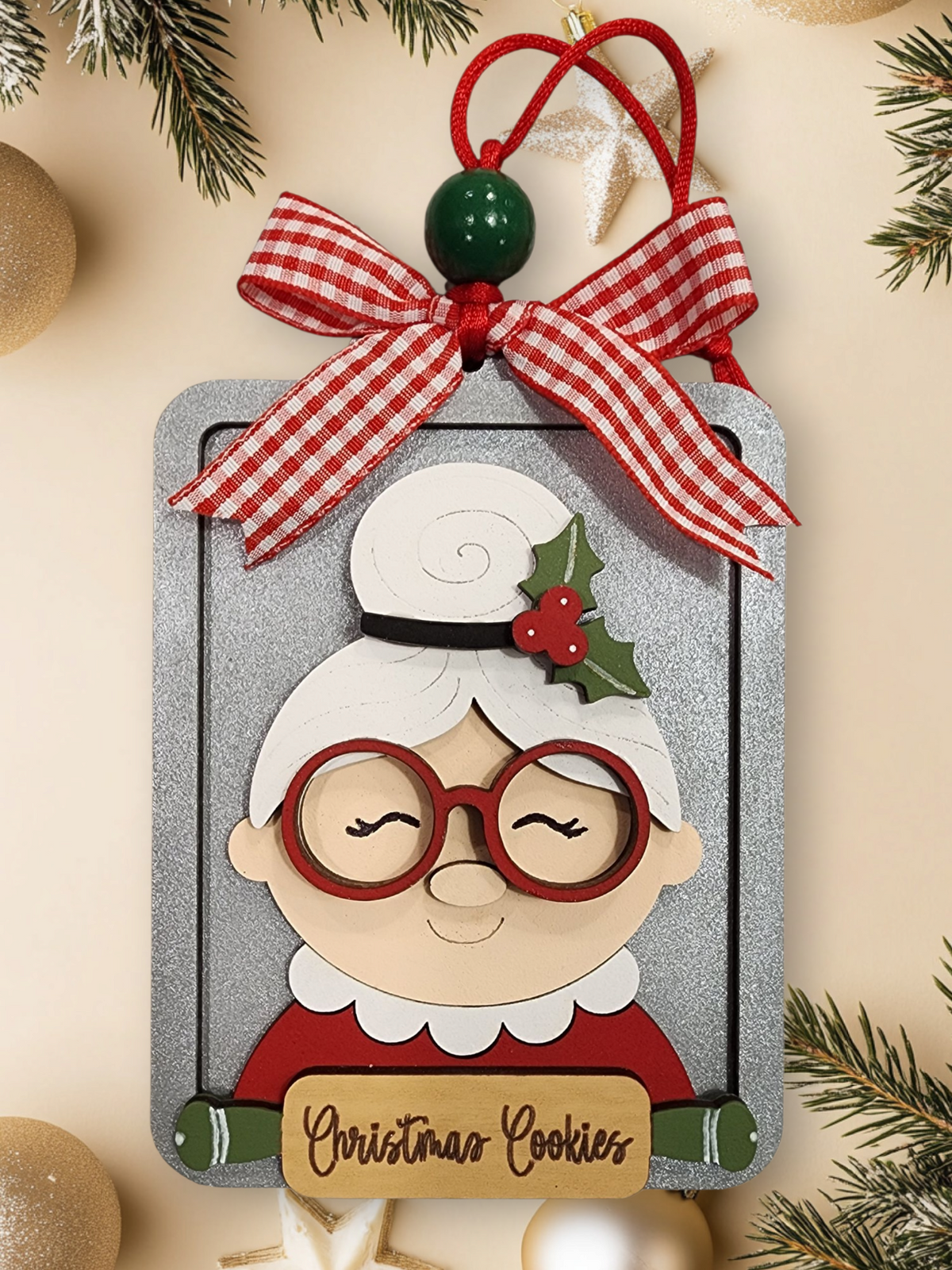 Decorative Christmas ornament with a mrs. Claus on a cookie sheet with a 'Christmas Cookies' written on a rolling pin. Topped off with a red and white checkered ribbon.